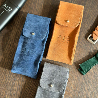 An assortment of colorful AIS Collective luxury leather watch pouches displayed together in a travel lifestyle setting.
