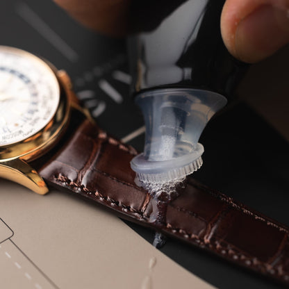 Applying specialized care formula directly to a premium brown leather watch strap using the integrated brush head.