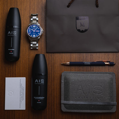 Flat lay of luxury watch accessories, including a blue dial watch alongside the AIS Collective ChronoPen, ChronoLeatherPen, and ChronoCloth.